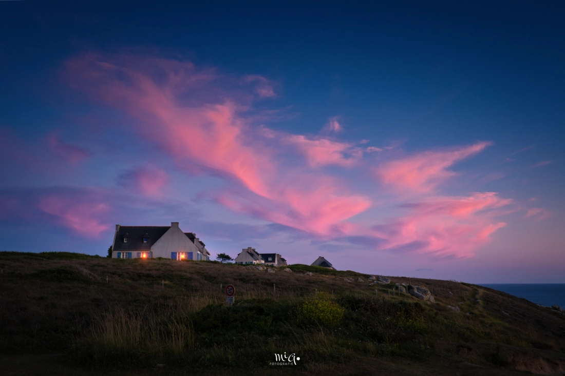 Bretonisches Kuestenhaus auf der Presqu'île de Crozon unter einem dramatischen Abendhimmel mit leuchtend rosa Wolken ueber dem Atlantik in der Bretagne