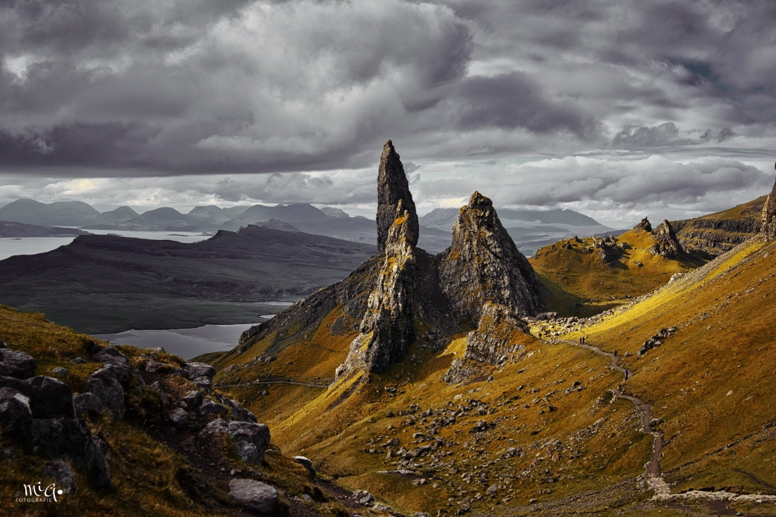 Die markanten Felsnadeln des Old Man of Storr auf der Isle of Skye unter dramatischem Wolkenhimmel mit goldenem Moosbewuchs und weitem Blick über die schottischen Highlands