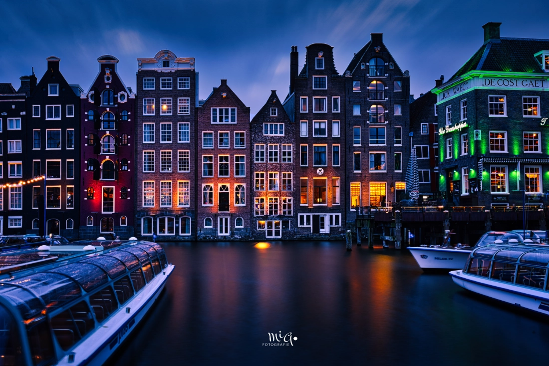 Amsterdam Grachtenhäuser bei Nacht – HDR Langzeitbelichtung Beleuchtete historische Grachtenhäuser in Amsterdam während der blauen Stunde mit spiegelglattem Wasser durch Langzeitbelichtung und ankernden Rundfahrtbooten.
